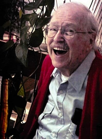 A 99-year-old man wearing glasses, a red sweater, and big smile.