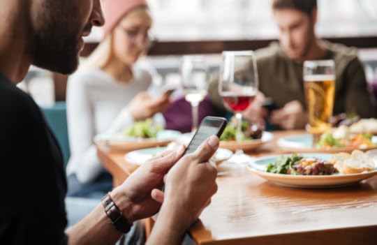 Group of men and women sitting around a table in a restaurant while shopping on their mobile phones to illustrate the concept of zero-click search