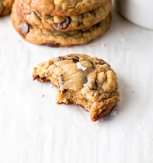 A up close photo of a half-eaten walnut chocolate chip cookie on a white surface.