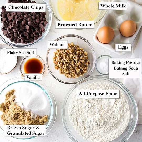 All of the ingredients you need to make walnut chocolate chip cookies portioned out in glass bowls on a white surface.