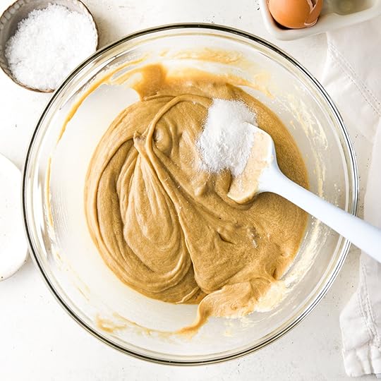 Baking powder, baking soda and salt getting mixed into cookie dough that looks tan and super creamy.