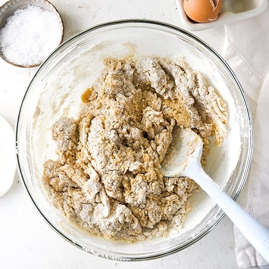 A dough that has flour just barely mixed into it in a glass bowl on a white surface.