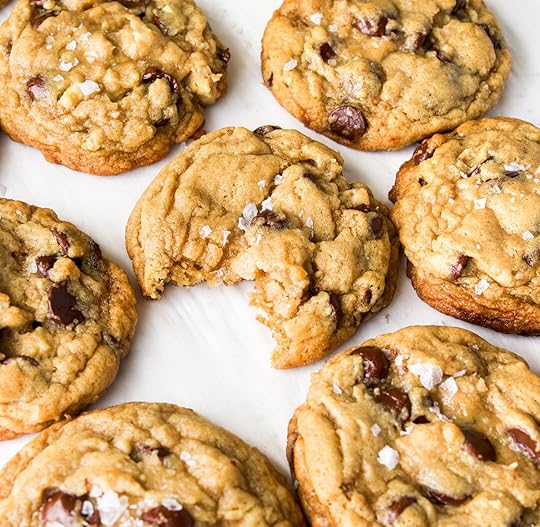 Walnut cookies with chocolate chips on a white surface with one cookie missing a bite.