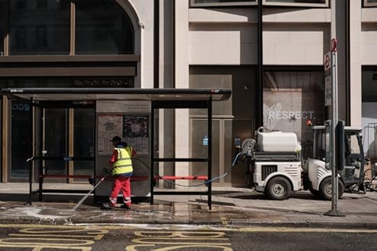 A man in red and hi-vis yellow with street cleaning apparatus on an urban pavement.