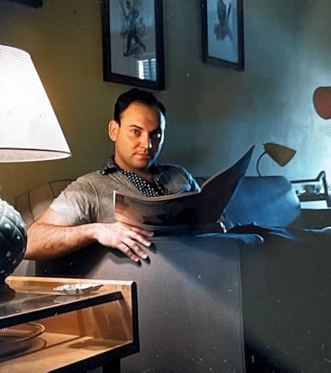 Maurice Zeldman as a young man. He is seated at a couch, a lamp beside him, in what appears to be a comfortable living room. The photographer appears to have surprised him while he was reading. His expression is fathomless.