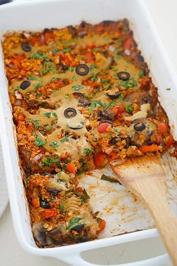 A casserole dish with pizza baked oats featuring red bell peppers, tomatoes, black olives, cheese, and spinach