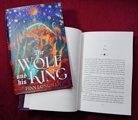 The Wolf and His King by Finn Longman, open to the first page of chapter 2, with another copy holding the book open.
