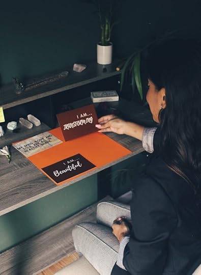 Woman arranging handwritten “I am” notes on a desk—how to make affirmation cards with simple supplies