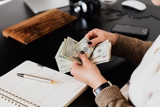 Person counting stacks of dollar bills at a desk, representing how can you increase your income with better money management