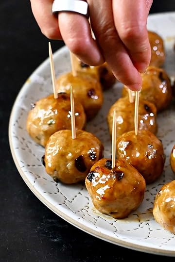 A hand is grabbing a cranberry turkey meatballs topped with a gluten free maple Dijon mustard glaze with a toothpick from a white plate.