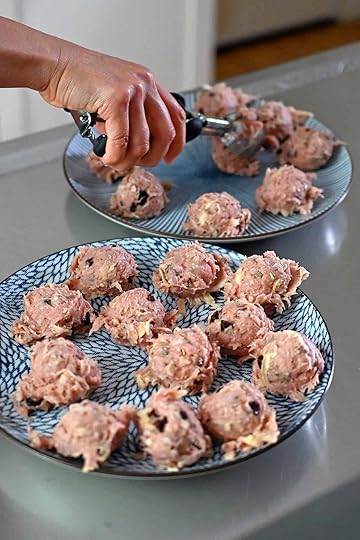 Portioning out 24 meatballs on two blue plates with a medium disher or ice cream scooper.