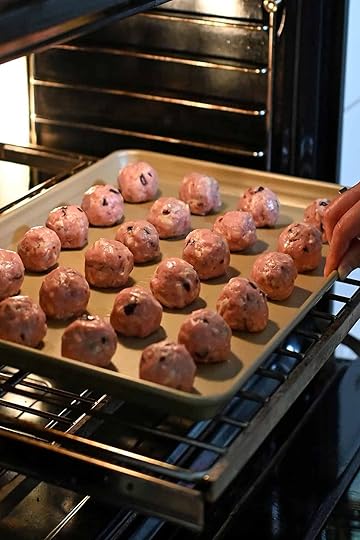 A hand is placing a tray of cranberry turkey meatballs into the oven to cook.