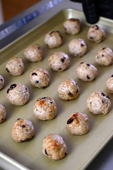 A rimmed baking sheet with baked cranberry turkey meatballs, right before a maple dijon mustard glaze is brushed on top.