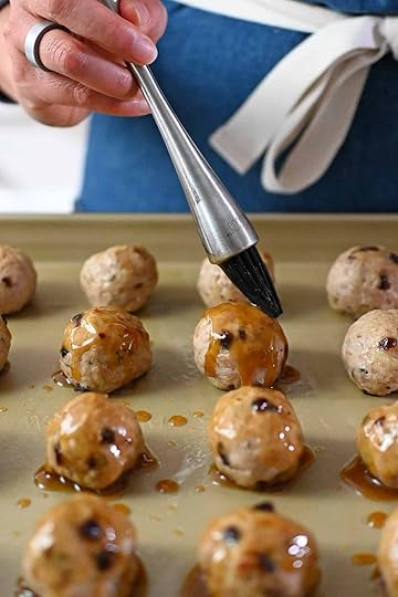 Brushing maple dijon glaze on cranberry turkey meatballs on a rimmed baking sheet.