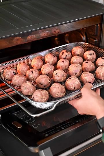 A hand is placing a wire mesh basket filled with raw cranberry turkey meatballs into a Breville Smart Oven Air fryer.