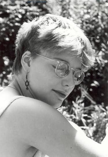 Sunlit BW photo of a woman wearing glasses and a women's sign earring. Her hair is messy and her eyes are closed.