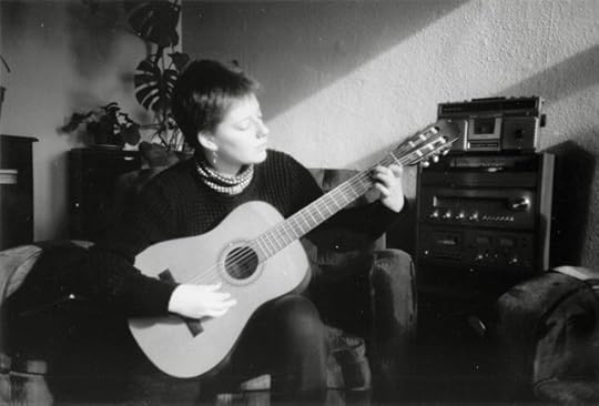 BW photo of very young white woman lit by slanting sun as she plays the acoustic guitar