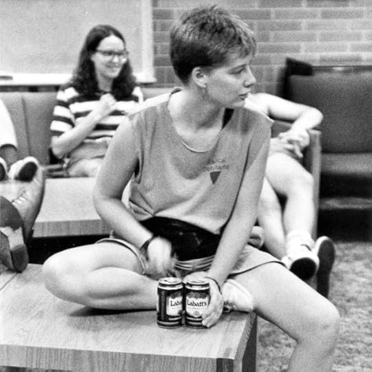 Young short-haired white woman in sleeveless tee shirt and shorts and playing percussion with a pen on two beer cans