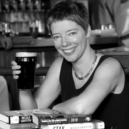 Smiling short-haired white woman in sleeveless vest sitting in a pub and raising a pint of Guinness