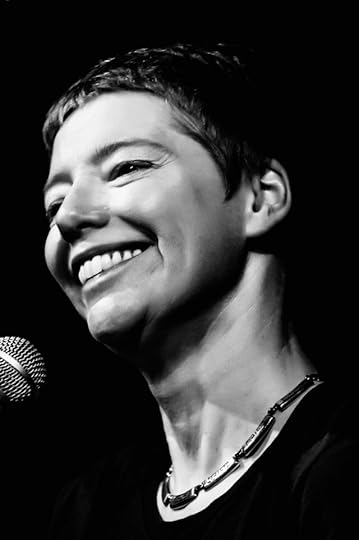 Black and white head shrt of a smiling, shrt-haired white woman before a microphone