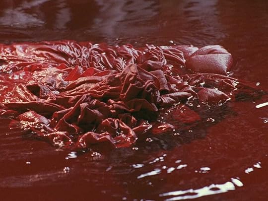 Red textiles float in a vat of dye in 