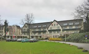 Exterior view of Hotel De Bilderberg in Oosterbeek, Netherlands, where the first Bilderberg Meeting was held in 1954. The building features a traditional architectural style with a surrounding green lawn and parked cars.