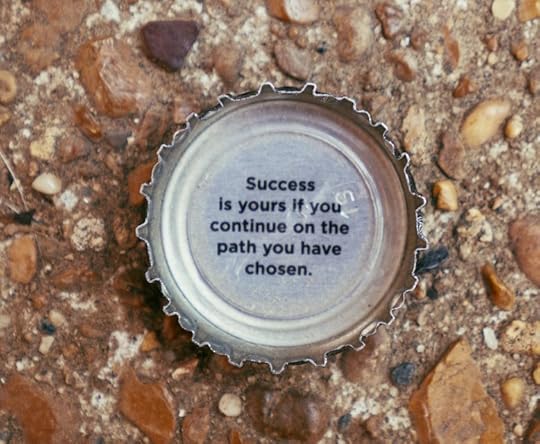 A bottle cap on the ground with the text 'Success is yours if you continue on the path you have chosen.'