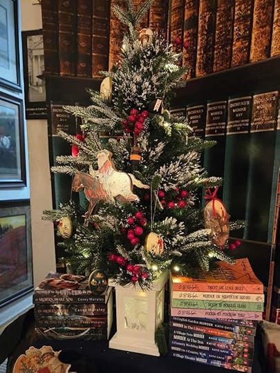 A stack of Milverton Mysteries paperback books under a small decorated Christmas tree
