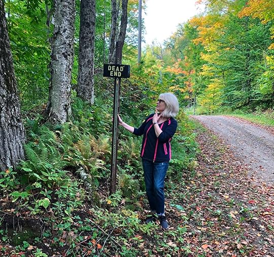 Woman standing on country road looking at a Dead End sign