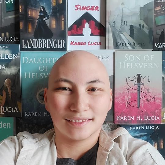 A smiling author with a shaved head poses in front of a collage of book covers, featuring titles from the Warriors of Helsvern series and others.