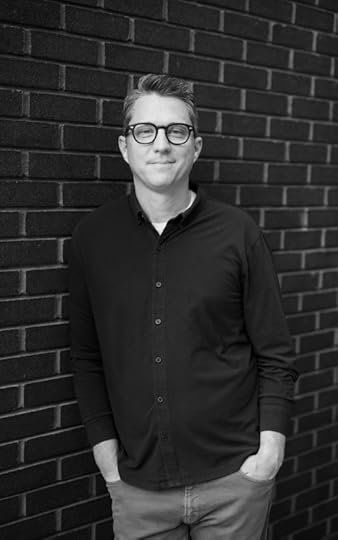 Matt Mooney poses for a black and white portrait against a brick wall.