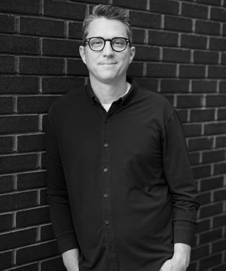 Matt Mooney poses for a black and white portrait against a brick wall.