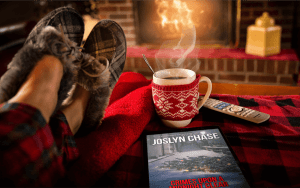 Enjoying Crimes Upon a Midnight Clear, by Joslyn Chase, with a cup of cocoa by the fireplace