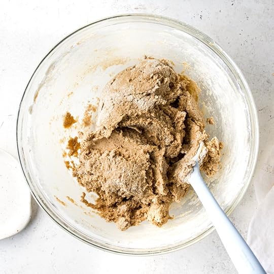 An overhead view of the finished soft and slightly shagging snickerdoodle cookie dough with flour streaks still visible and a spatula resting inside the glass bowl.