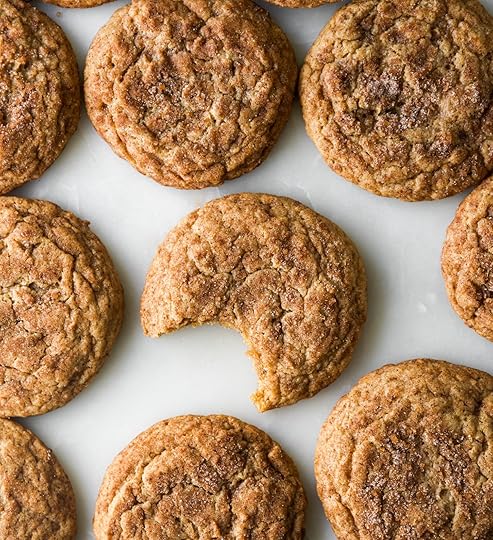Ann overhead view of nine round golden brown chai snickerdoodle cookies arrange on a white marble surface. The center cookie has a bite taken out of it showing the soft, chewy interior and the crinkled texture of the cinnamon sugar coating.
