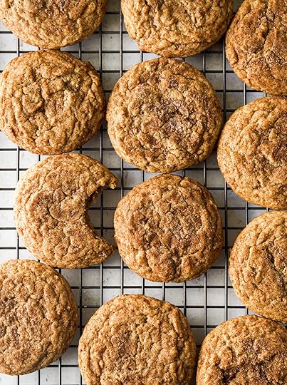 An overhead shot of multiple round, golden brown dirty chai snickerdoodle cookies cooling on a black wire rack. One cookie on the left side has a large bite taken out of it revealing a soft light brown interior and crinkle top exterior.