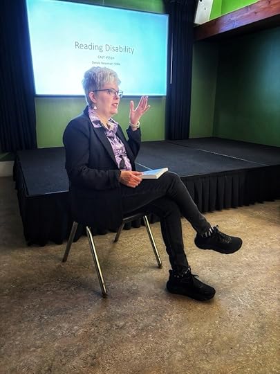 I’m sitting in a chair gesturing while I answer a student’s question. Behind me is a screen displaying the text: Reading Disability