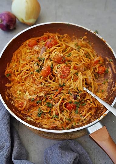 A pan filled with creamy onion pasta, mixed with cherry tomatoes and herbs, sits on a gray cloth