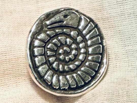 Snakestone cast in silver to form a pin, resting against natural linen
