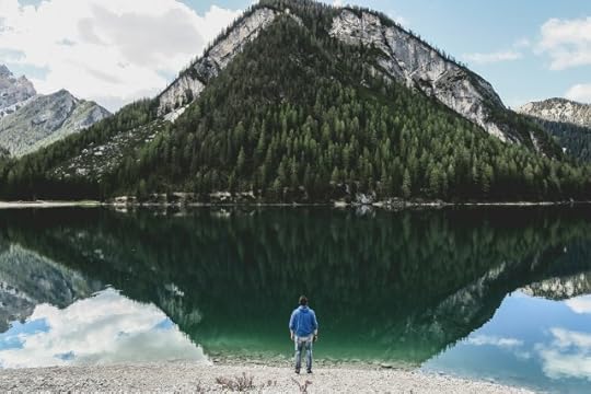 A man observing a mountain reflected in a lake. Stillness, reflection, and positivity