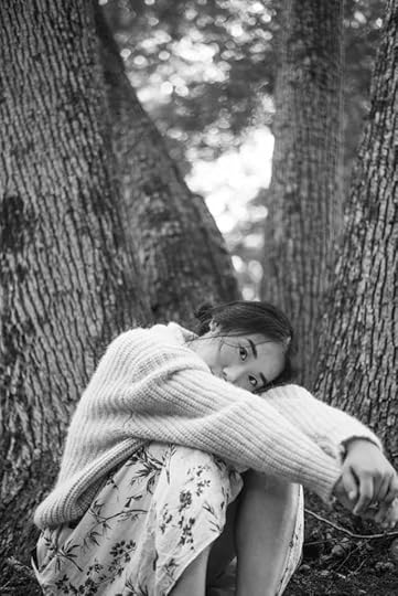 Current image: ethnic woman sitting leaning down in front of tree trunks