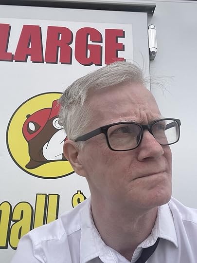 An author headshot of a white man with short grey hair and black framed glasses looking off into the top right of the picture.
