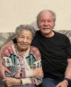 Elderly woman seated on couch beside middle-aged man with moustache