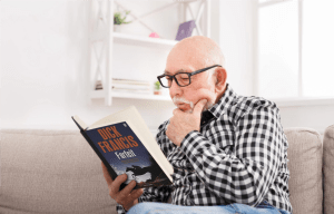 Older fellow on couch, absorbed in reading Forfeit, by Dick Francis