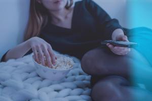 Woman watching TV with remote in hand and eating popcorn from a bowl