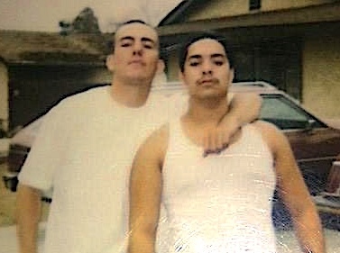 2 men standing next to on another with one man's arm over the shoulder of the other.