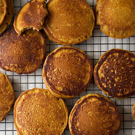 Overhead shot of multiple freshly cooked fluffy pumpkin pancakes cooling on a metal wire rack, showing the golden brown color and airy texture. One pancake has a bite taken out of it.