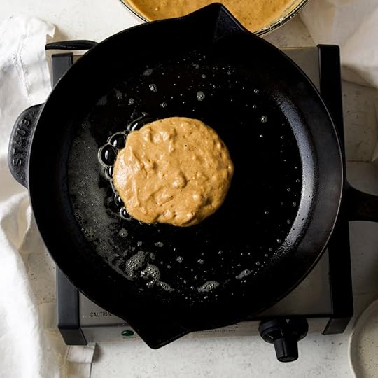 Pumpkin pancake batter being dropped onto a hot cast iron skillet coated with melted butter, showing the pancake beginning to cook.