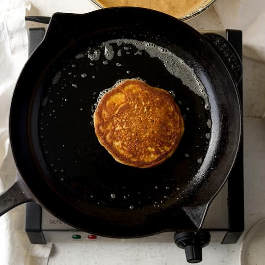 A single fluffy pumpkin pancake cooking in a sizzling cast iron skillet, with a perfectly golden brown top after being flipped.