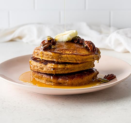 Stack of homemade pumpkin pancakes topped with butter, maple syrup and pecans on a pink plate.